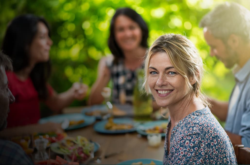 A woman smiling while sitting at a table with other people.