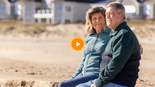 Video thumbnail of an older couple sitting on a beach.